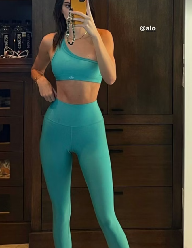 Kendall Jenner taking a selfie in a bright green ALO Yoga sports bra and leggings set.
