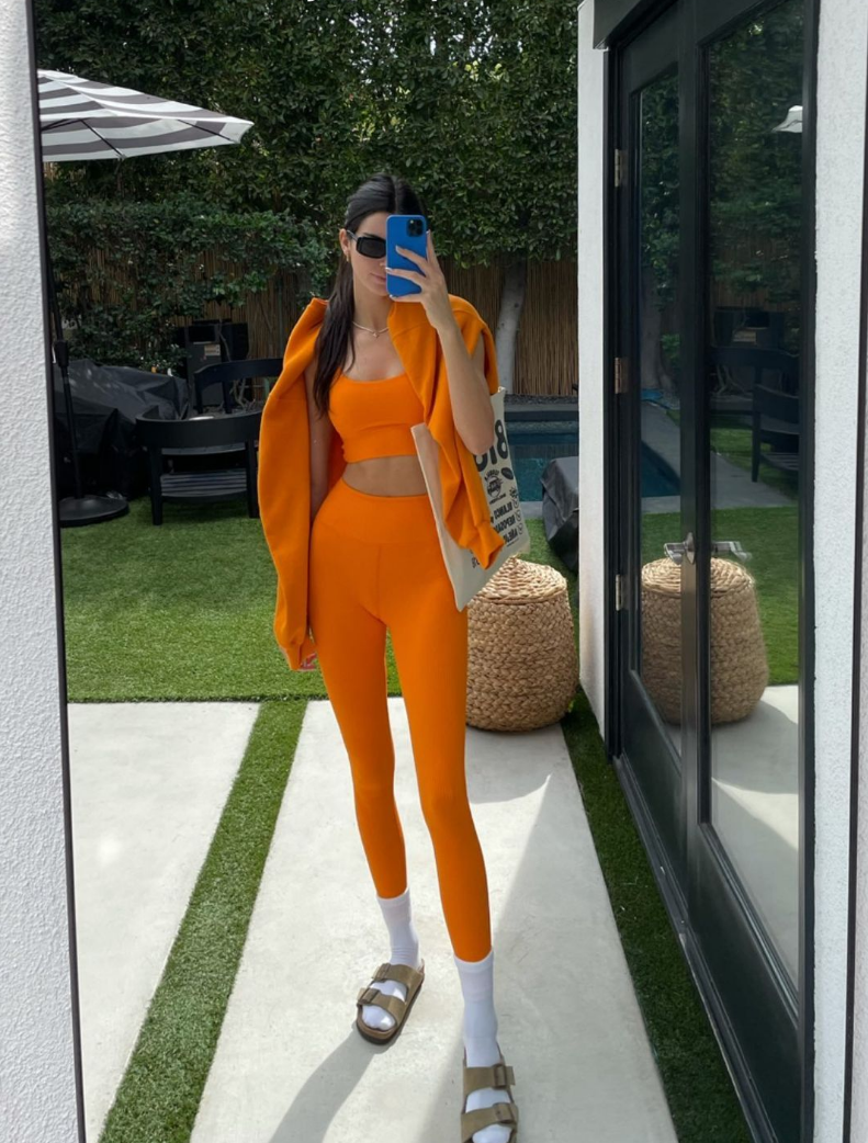 Kendall Jenner taking a selfie in an orange Year of Ours sports bra and leggings set.