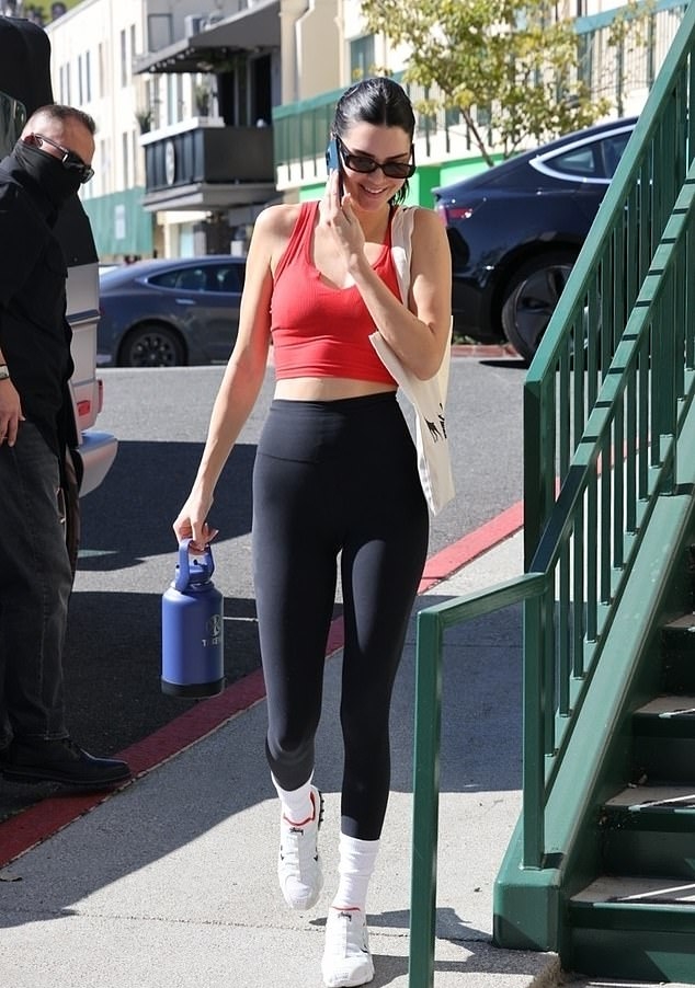 Kendall Jenner taking a selfie in an orange Revolve sports bra and leggings set.