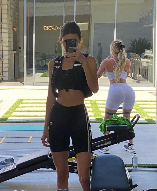 Kendall Jenner taking a selfie during backyard workout in a black adidas sports bra and legging shorts set.